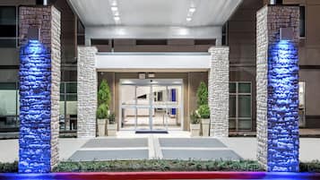 A hotel entrance with stone pillars, glass doors, and a red curb.
