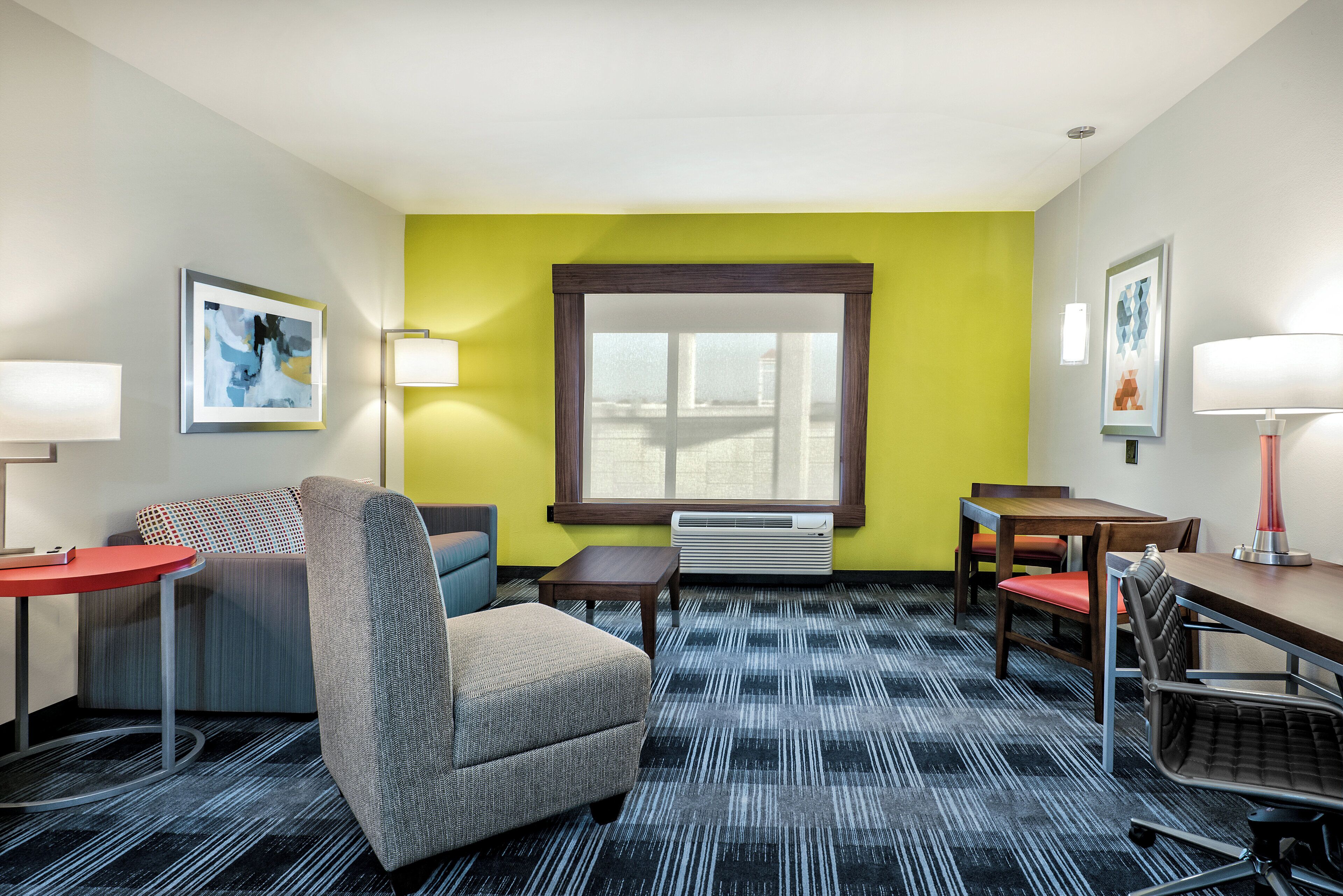 A hotel room with a sofa, armchair, small table, and a desk with chairs.