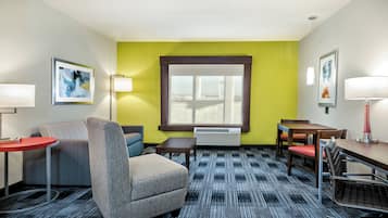 A hotel room with a sofa, armchair, small table, and a desk with chairs.