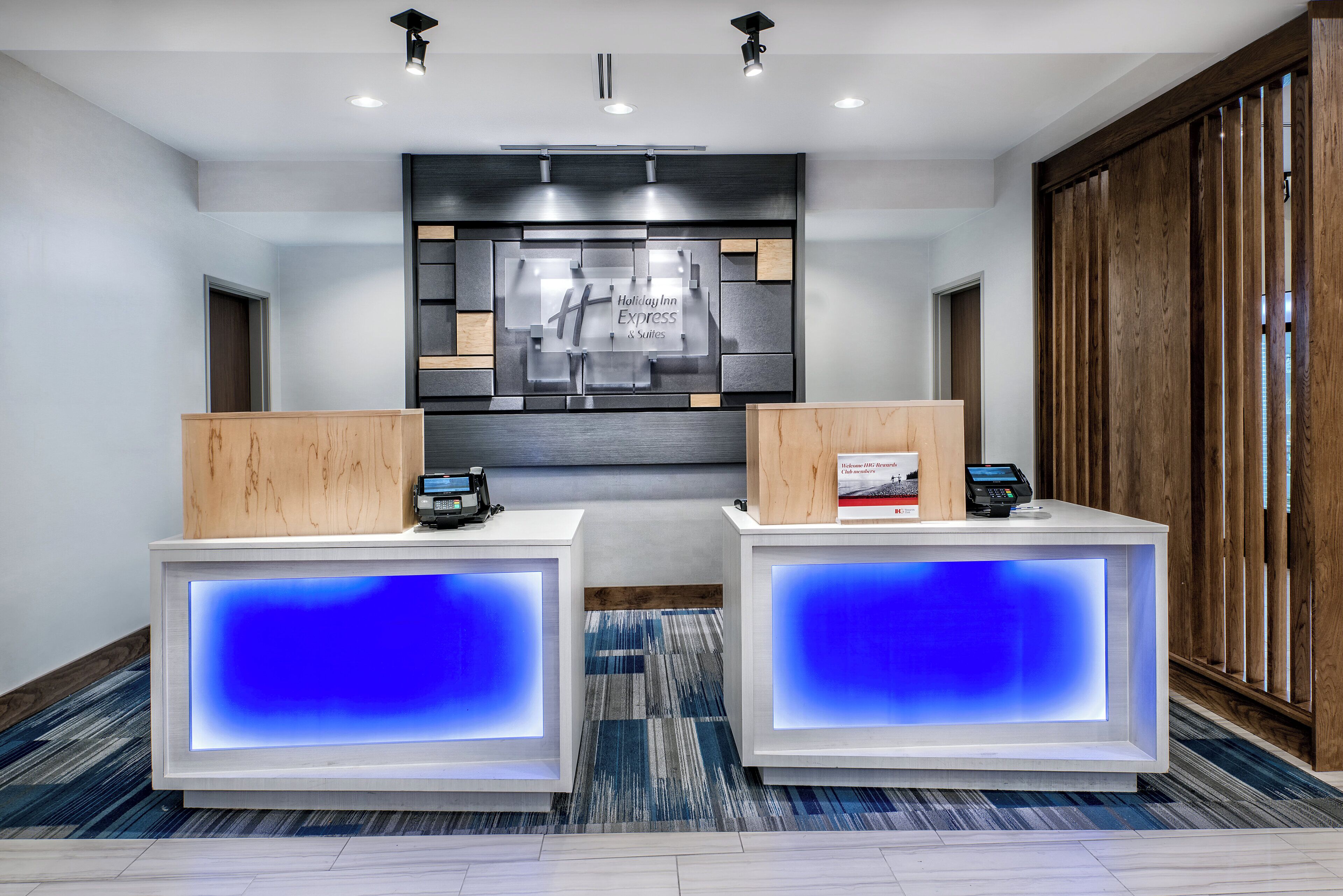 A hotel reception area with two reception desks, a digital display, and a wall-mounted sign.
