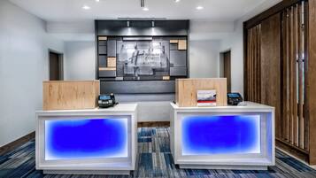 A hotel reception area with two reception desks, a digital display, and a wall-mounted sign.