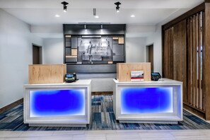 A hotel reception area with two reception desks, a digital display, and a wall-mounted sign. - Holiday Inn Express & Suites Austin - Round Rock Area by IHG (Austin)