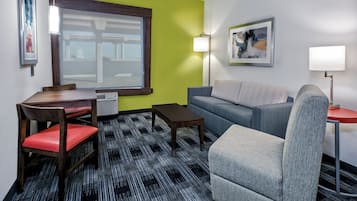 A compact living space with a dining table, chairs, a sofa, and a patterned carpet.