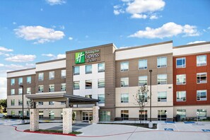 A Holiday Inn Express & Suites hotel with a modern design, featuring a prominent sign, a covered entrance, and a parking area with handicapped accessibility.
