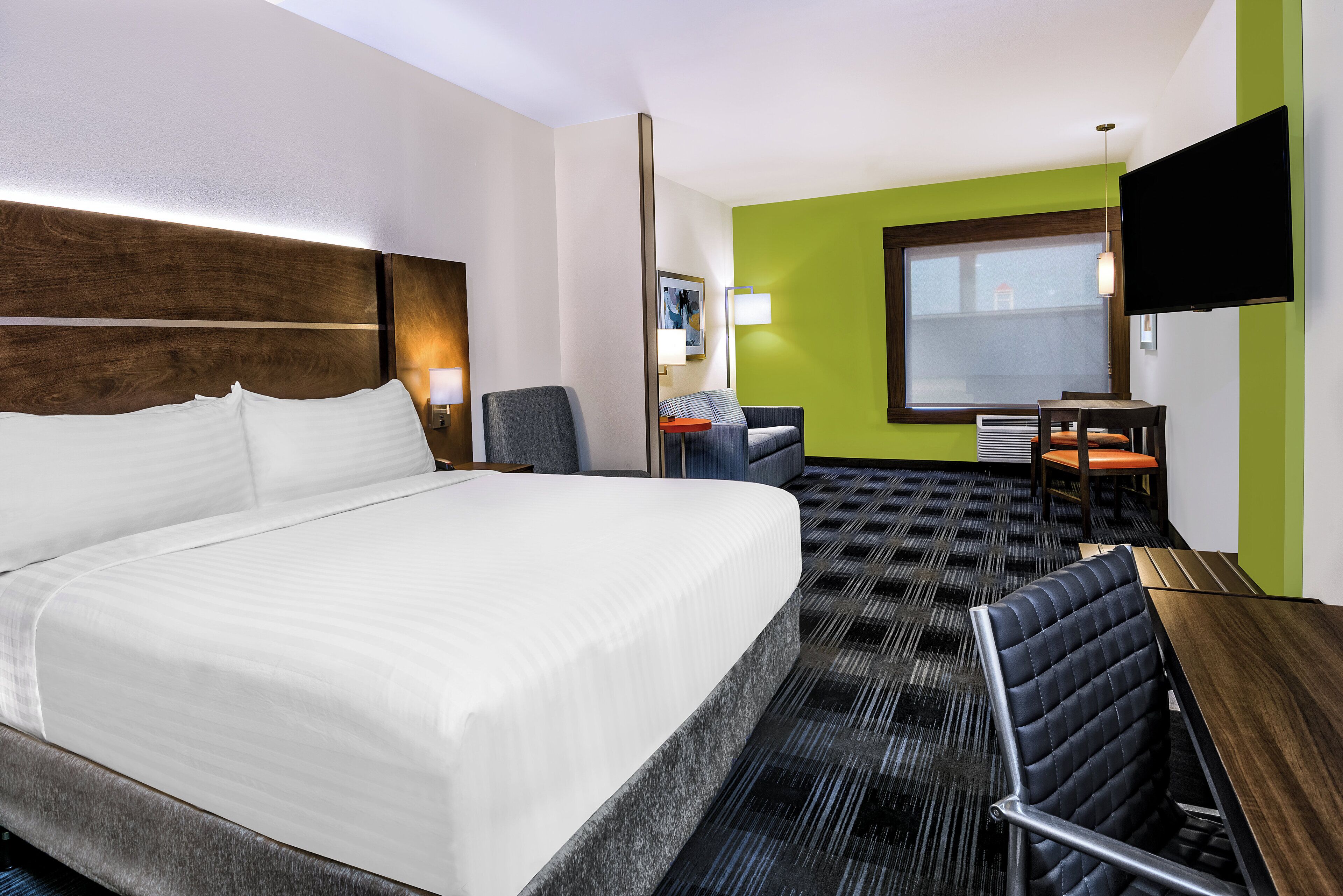 A hotel room with a large bed, a desk, a chair, a television, and a window.