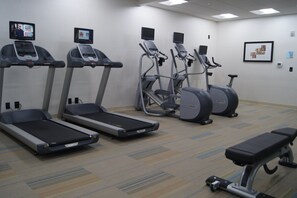 A fitness room with treadmills, elliptical machines, and a bench.