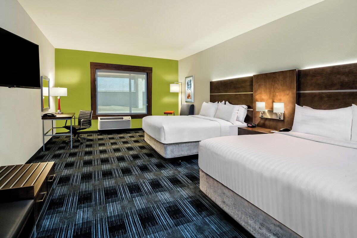A hotel room with two beds, a desk, a chair, a TV, and a window.