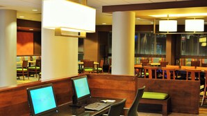 Un vestíbulo de hotel con estaciones de trabajo por computadora, zonas de estar y ventanas amplias.
