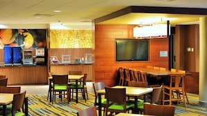 Un comedor de hotel con mesas y sillas de madera, una barra con una máquina de café y un televisor montado en la pared.