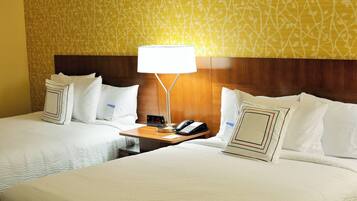 A hotel room with two beds, a nightstand with a lamp, a clock, and a phone.