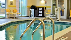 Una piscina interior con agua cristalina, escaleras de metal y sillas amarillas alrededor de la zona de la piscina.