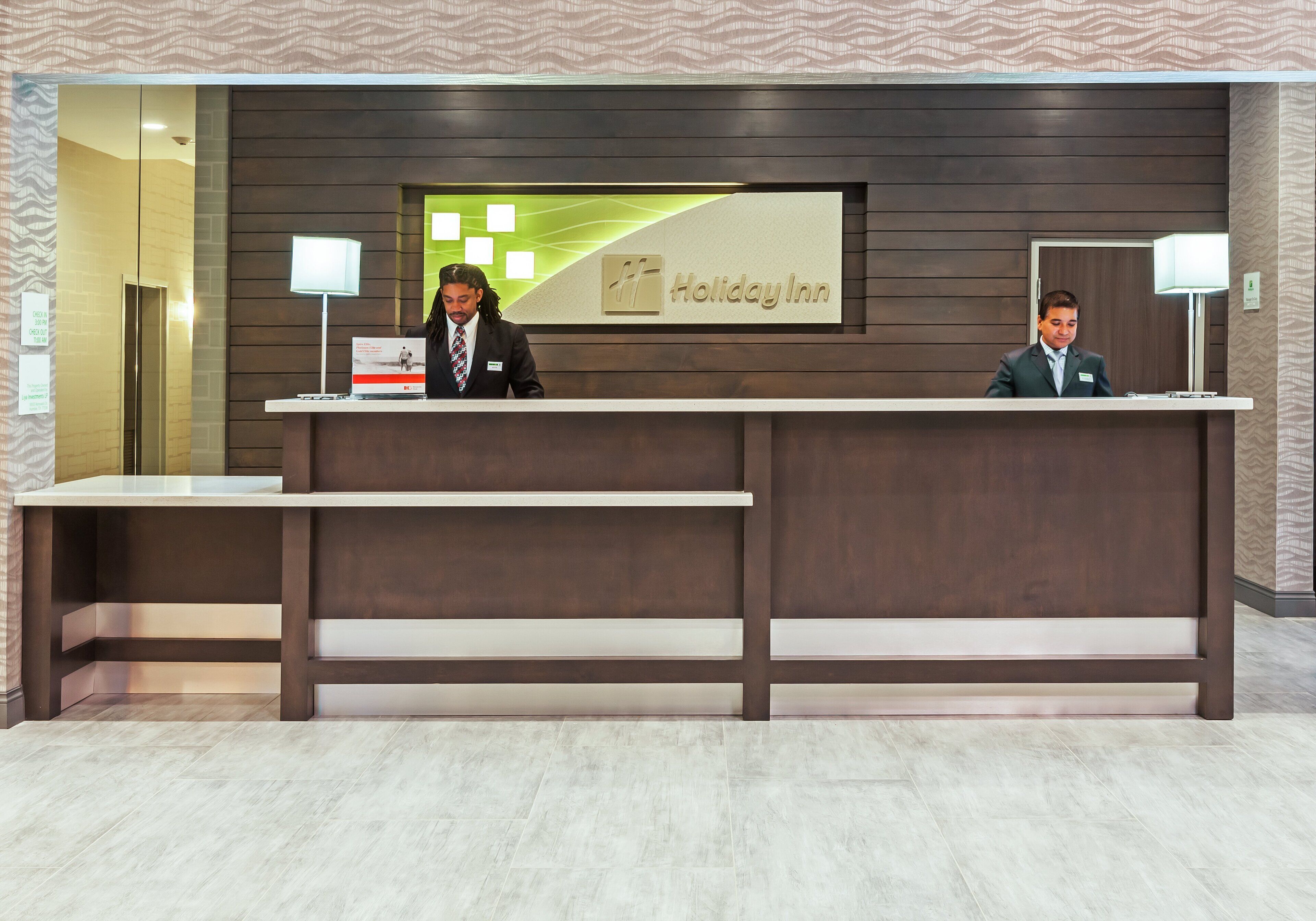 A reception desk at Holiday Inn with a modern design, a digital screen, and two receptionists.