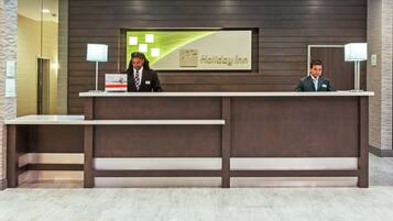 A reception desk at Holiday Inn with a modern design, a digital screen, and two receptionists.