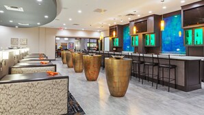 Un espace bar moderne avec des tabourets hauts, un long comptoir et un coin salon agrémenté de coussins à motifs.