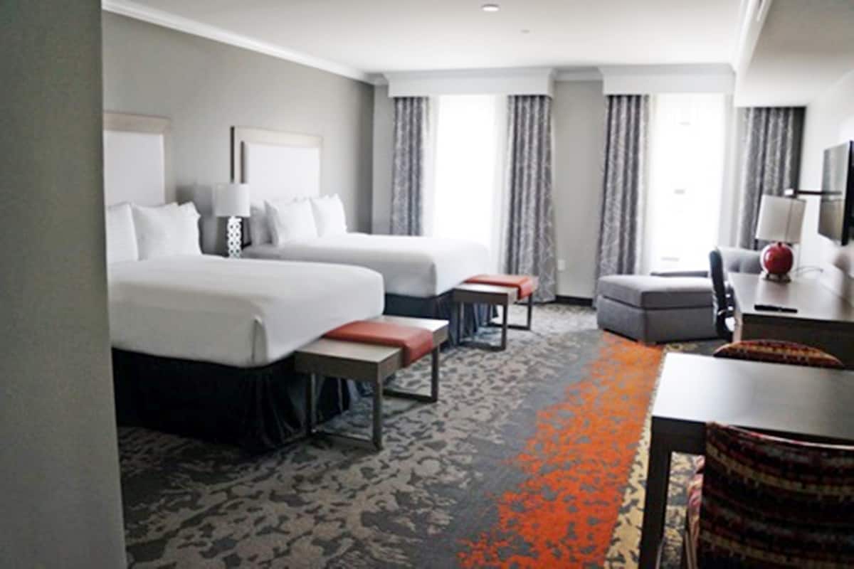 A hotel room with two beds, a desk, a chair, a small table, and a sofa.