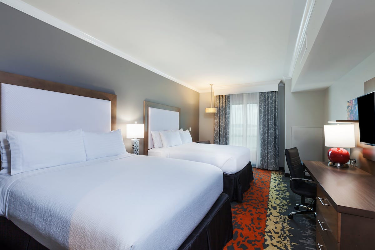 A hotel room with two beds, a desk, and a TV.