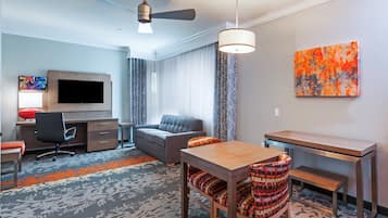 A hotel room with a sofa, a dining table, a TV, a desk, and a ceiling fan.