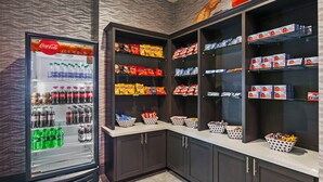 Un espace de vente proposant des collations et des boissons, avec un réfrigérateur Coca-Cola, des étagères remplies de chips et d’autres en-cas, et des paniers pour les articles supplémentaires.