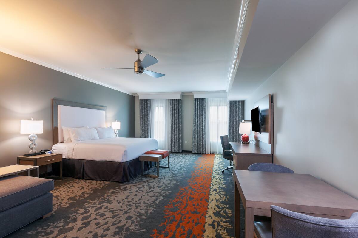 A hotel room with a bed, desk, chair, and a television.