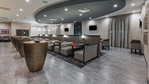Un hall d’hôtel moderne doté d’un plafond incurvé, d’un éclairage encastré et d’un espace détente avec des tables et des chaises.