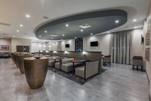 Un moderno vestíbulo de hotel con techo curvo, iluminación empotrada y una zona de estar con mesas y sillas.