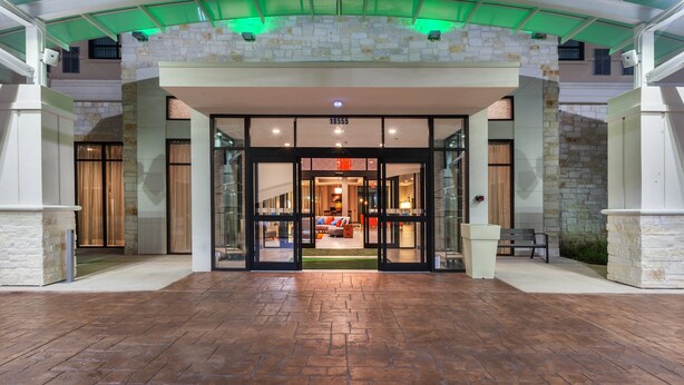 A hotel entrance with a stone facade, glass doors, and a number sign '18555'. - Holiday Inn Houston NE - Bush Airport Area by IHG (Humble)