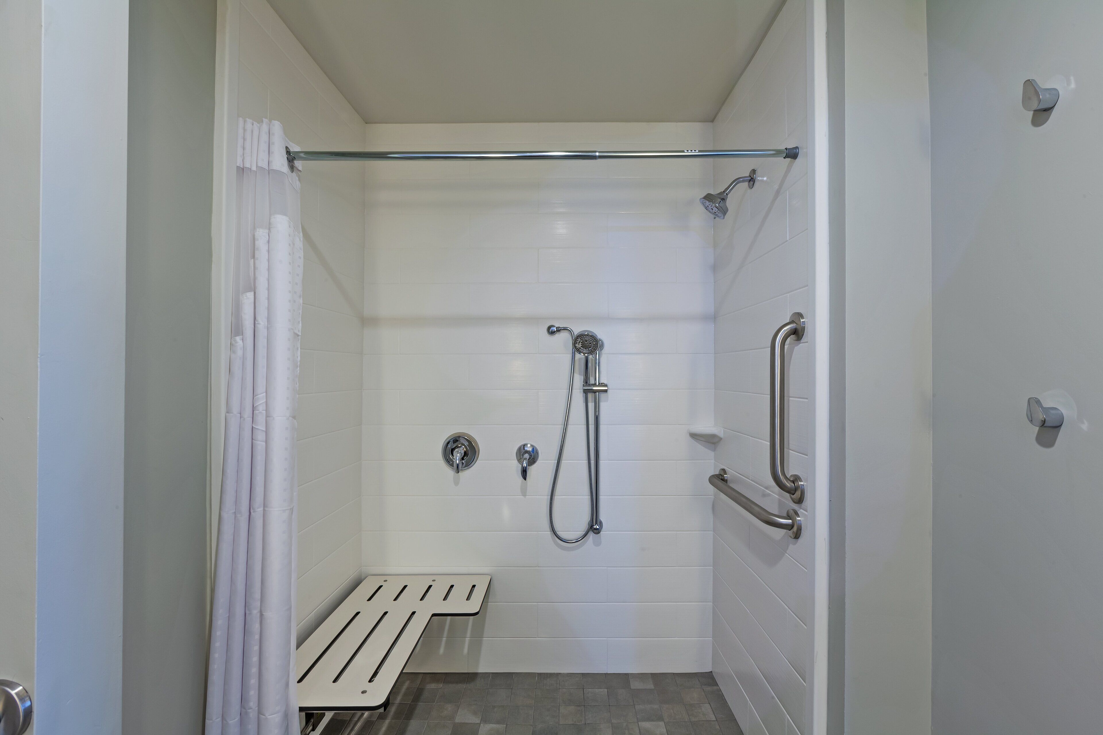 A small, enclosed shower area with a bench, grab bars, and a showerhead.