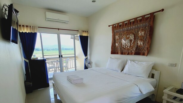 Habitación de hotel con una cama grande, un balcón con mesa y sillas, un aire acondicionado y un tapiz en la pared.