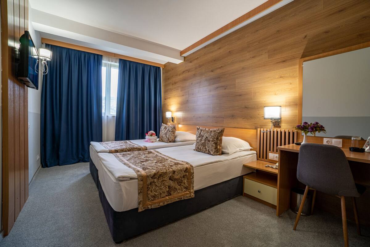 A hotel room with a large bed, a desk, a chair, a TV, and a wooden accent wall.