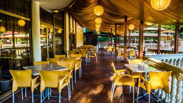 A restaurant with yellow chairs and tables, large windows, and hanging paper lanterns.