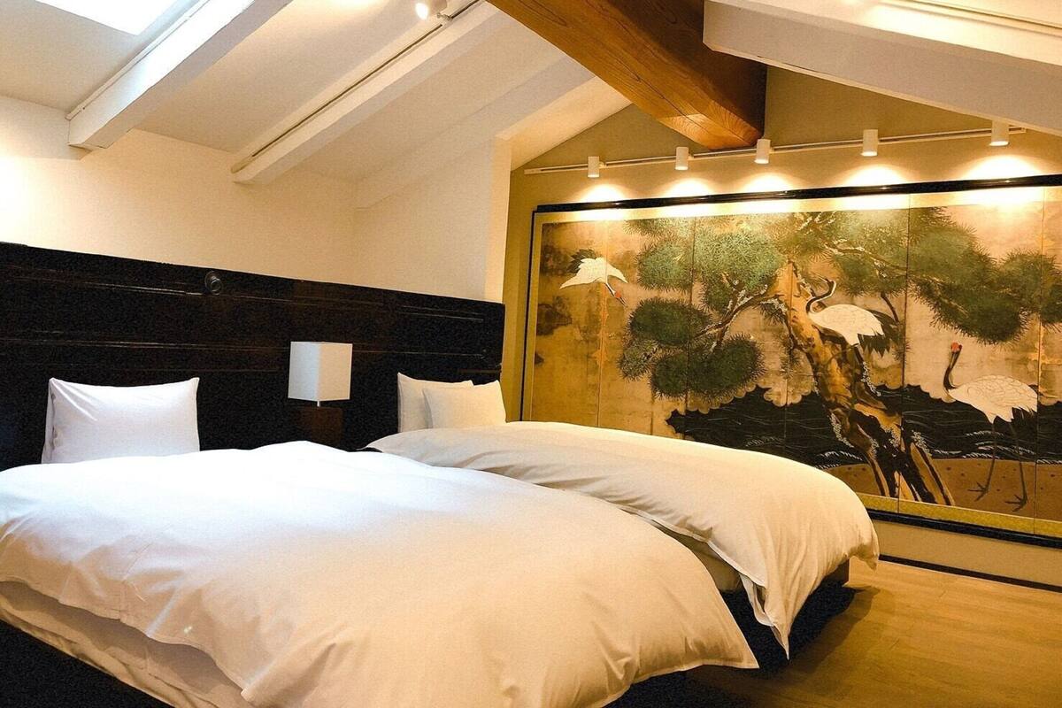 A bedroom with a large bed, wooden beams, a skylight, and a traditional painting on the wall.