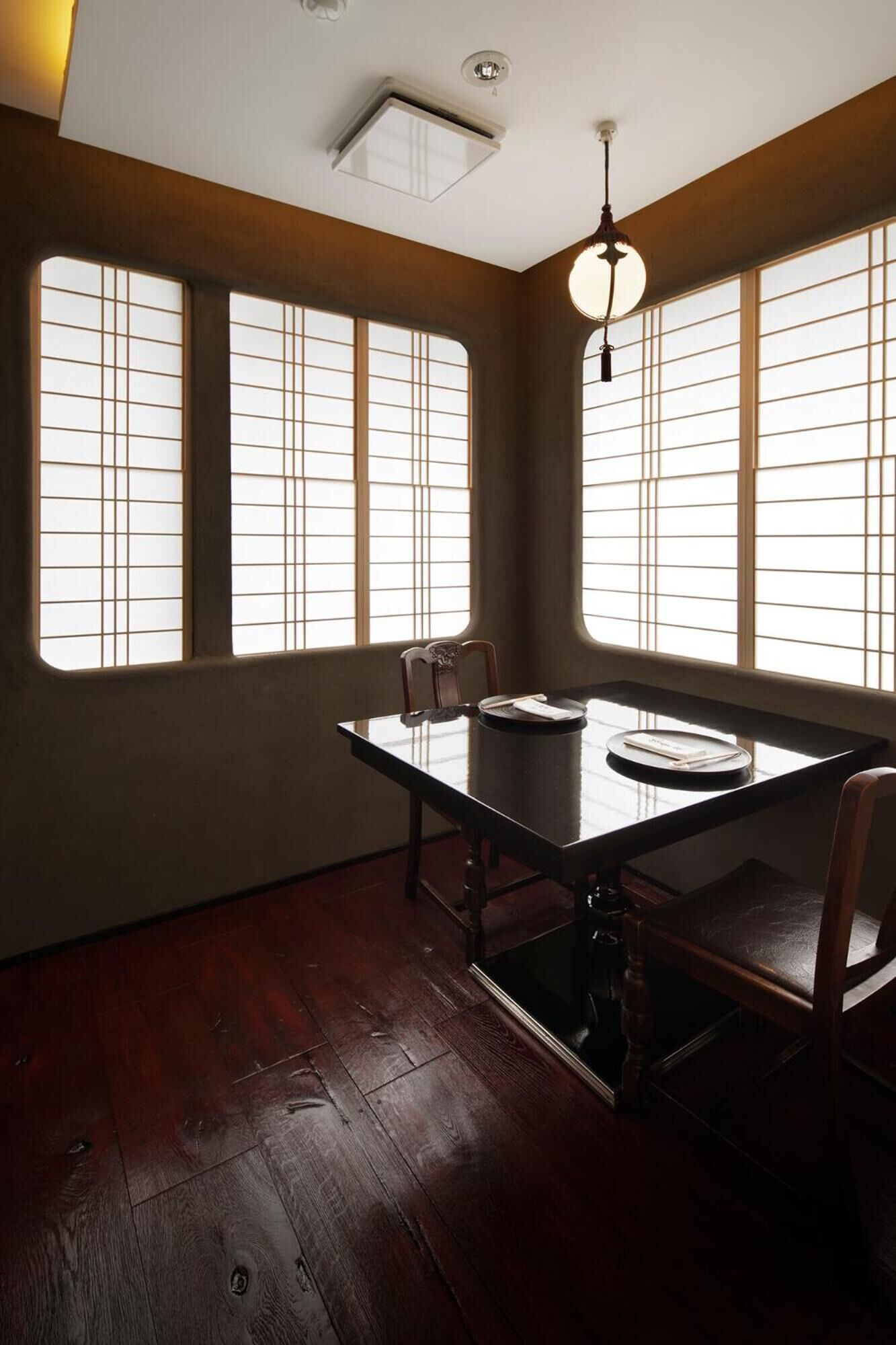 A dining area with a table and chairs, large windows with blinds, and a ceiling light fixture.