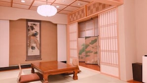 Une pièce de style japonais traditionnel, avec un sol recouvert de tatamis, une basse table en bois, une œuvre d’art suspendue et des portes coulissantes.