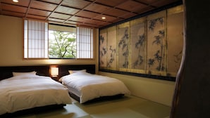 Une pièce de style japonais traditionnel, avec un sol recouvert de tatamis, deux lits, un paravent shoji orné de motifs en bambou et une fenêtre donnant sur la forêt.