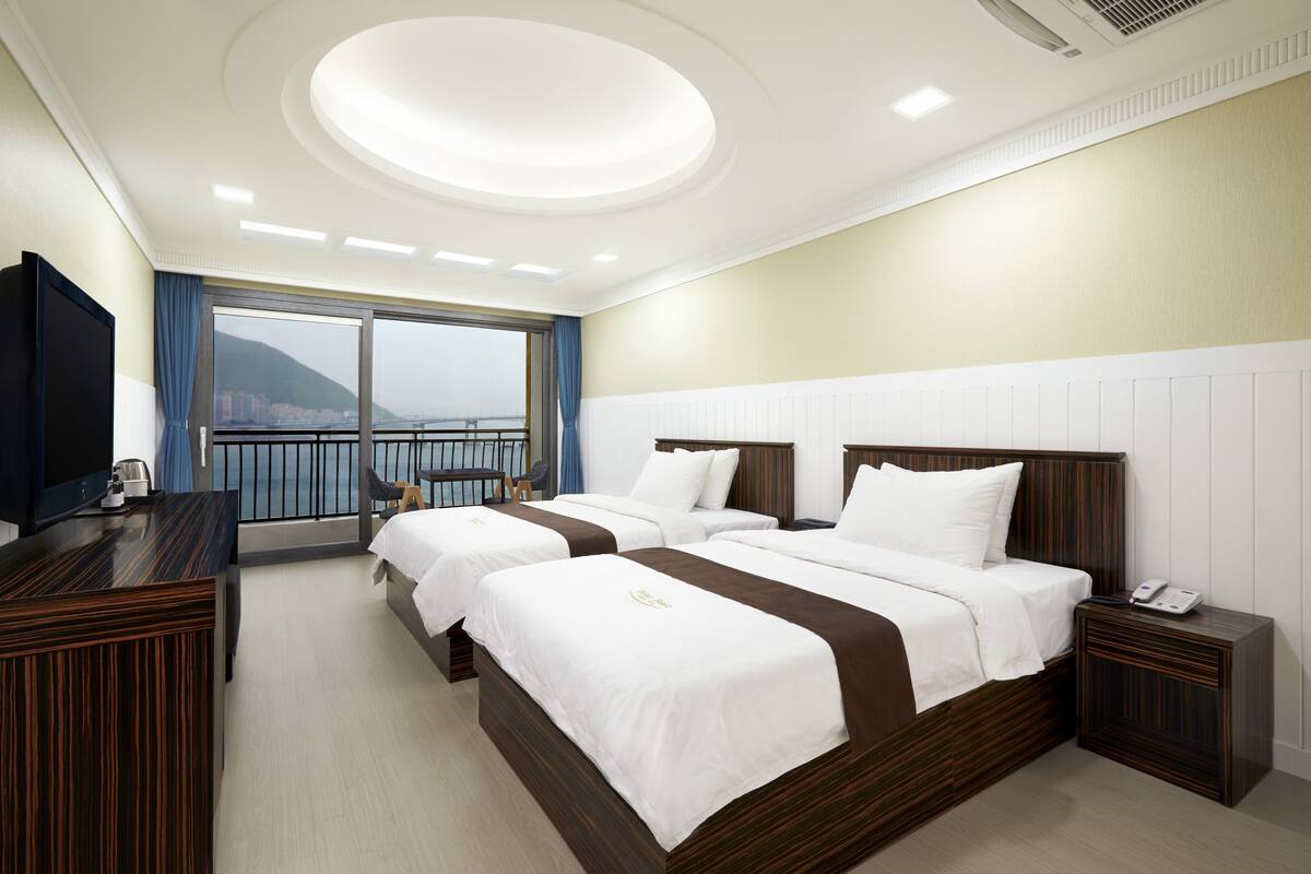 Ein Hotelzimmer mit zwei Betten, einem Schreibtisch, einem Fernseher und einem Balkon mit Blick.