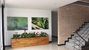 A modern interior with a wooden planter with red flowers, two bird paintings on the wall, and a staircase with a metal railing. - Nogal Hotel (La Ceja)