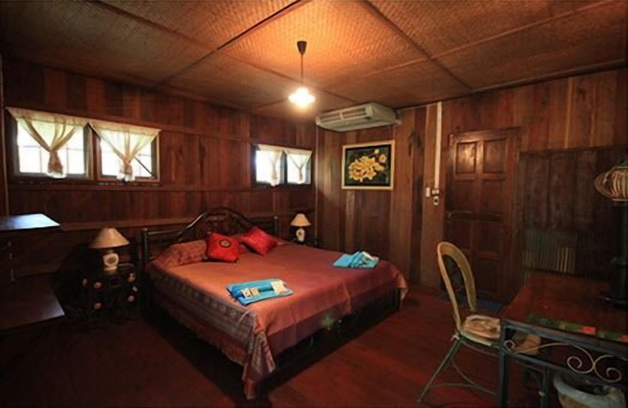 A wooden room with a bed, a chair, a table, and a window with curtains.