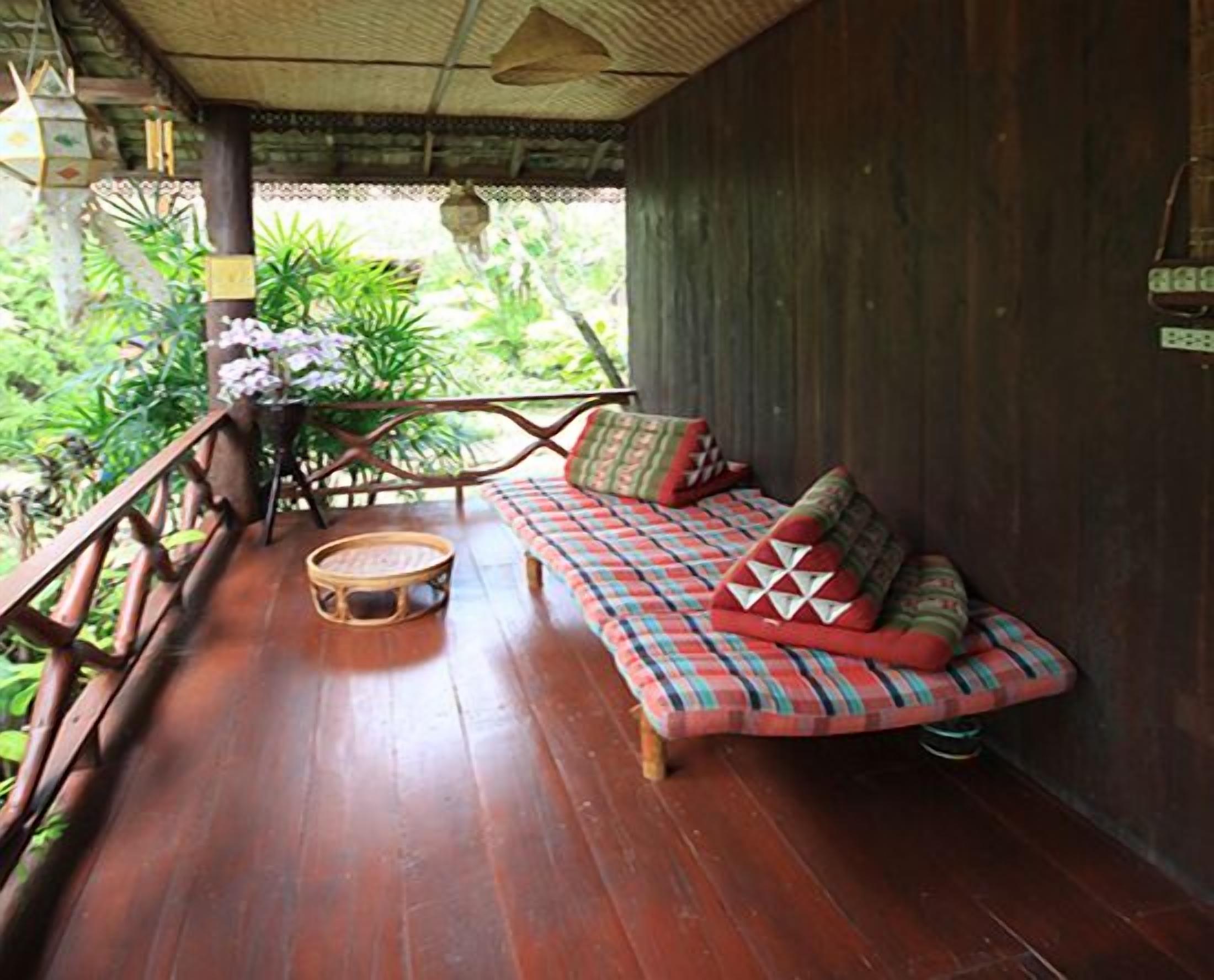 A wooden deck with a sofa and a round table, surrounded by lush greenery.
