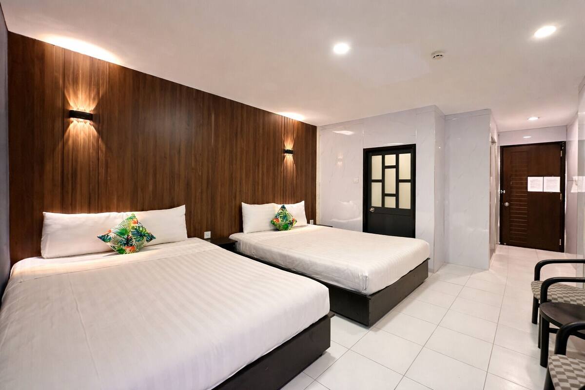 Une chambre d’hôtel avec deux lits, un mur décoratif en bois, une porte noire et une chaise à carreaux.