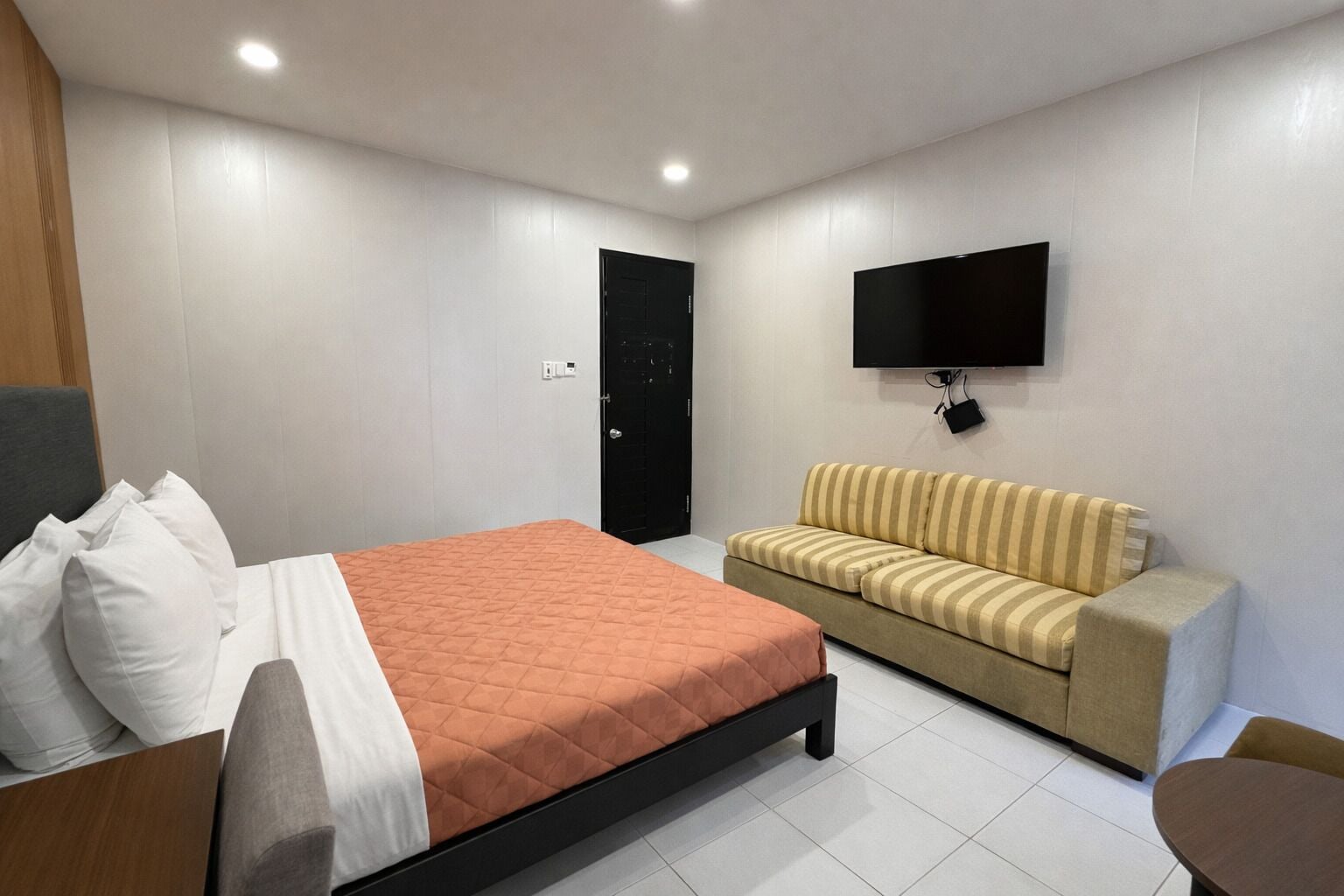 Een moderne slaapkamer met een bed, een bank, een televisie en een deur.