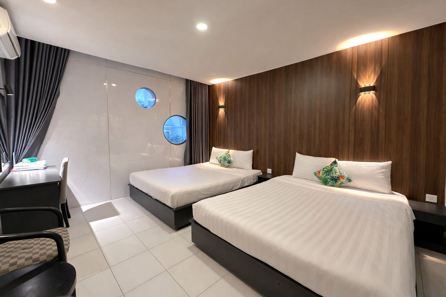 A modern hotel room with two beds, a desk, and a chair.