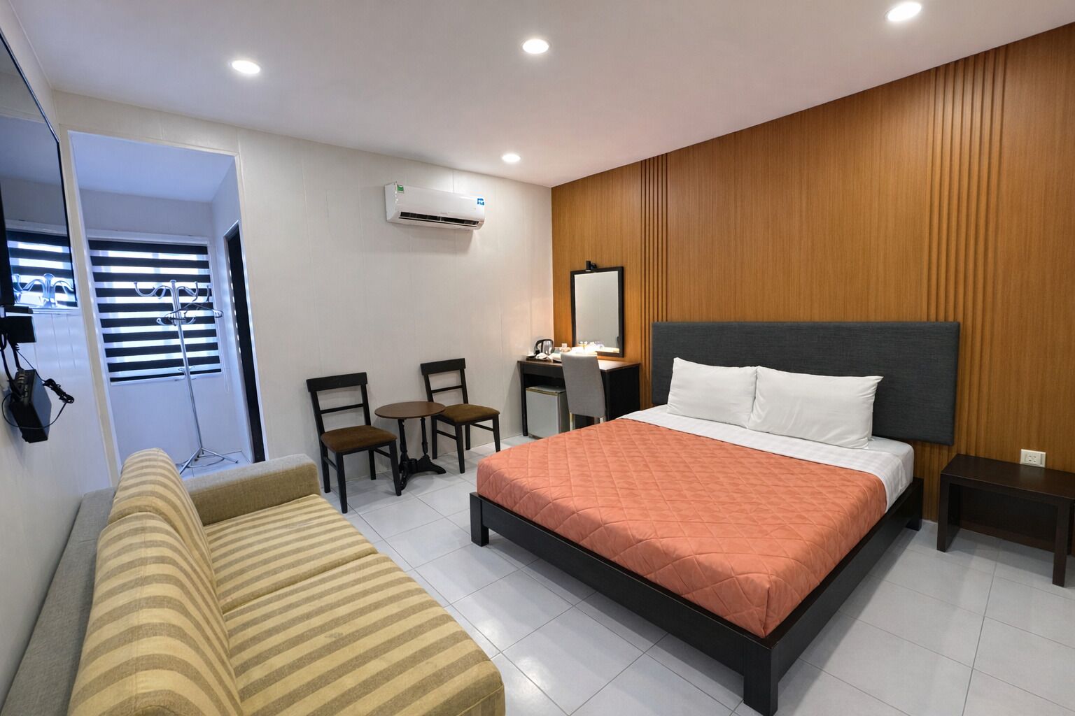 A hotel room with a bed, a desk, two chairs, a sofa, and a mirror.