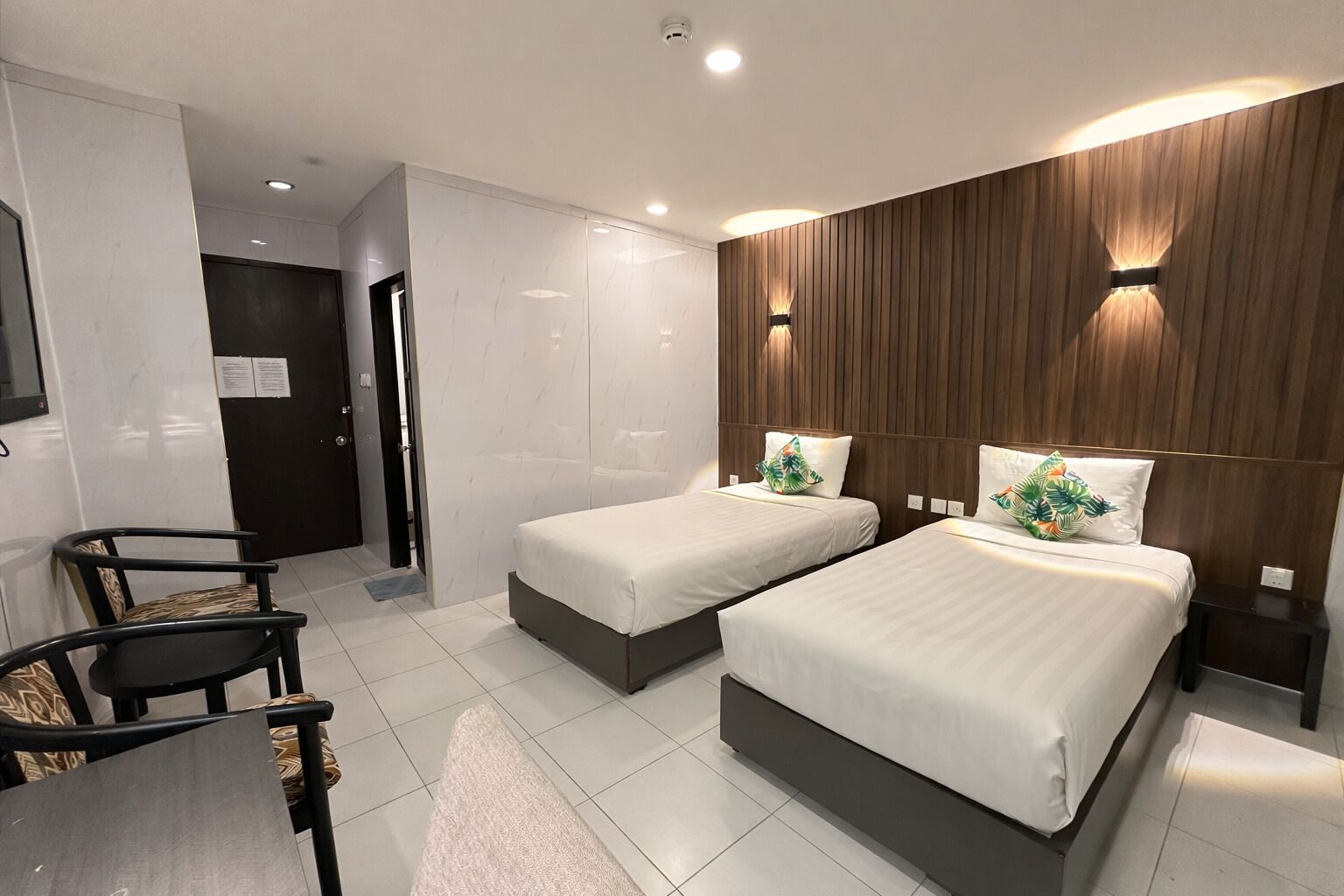 A modern hotel room with two single beds, a desk, and a chair.
