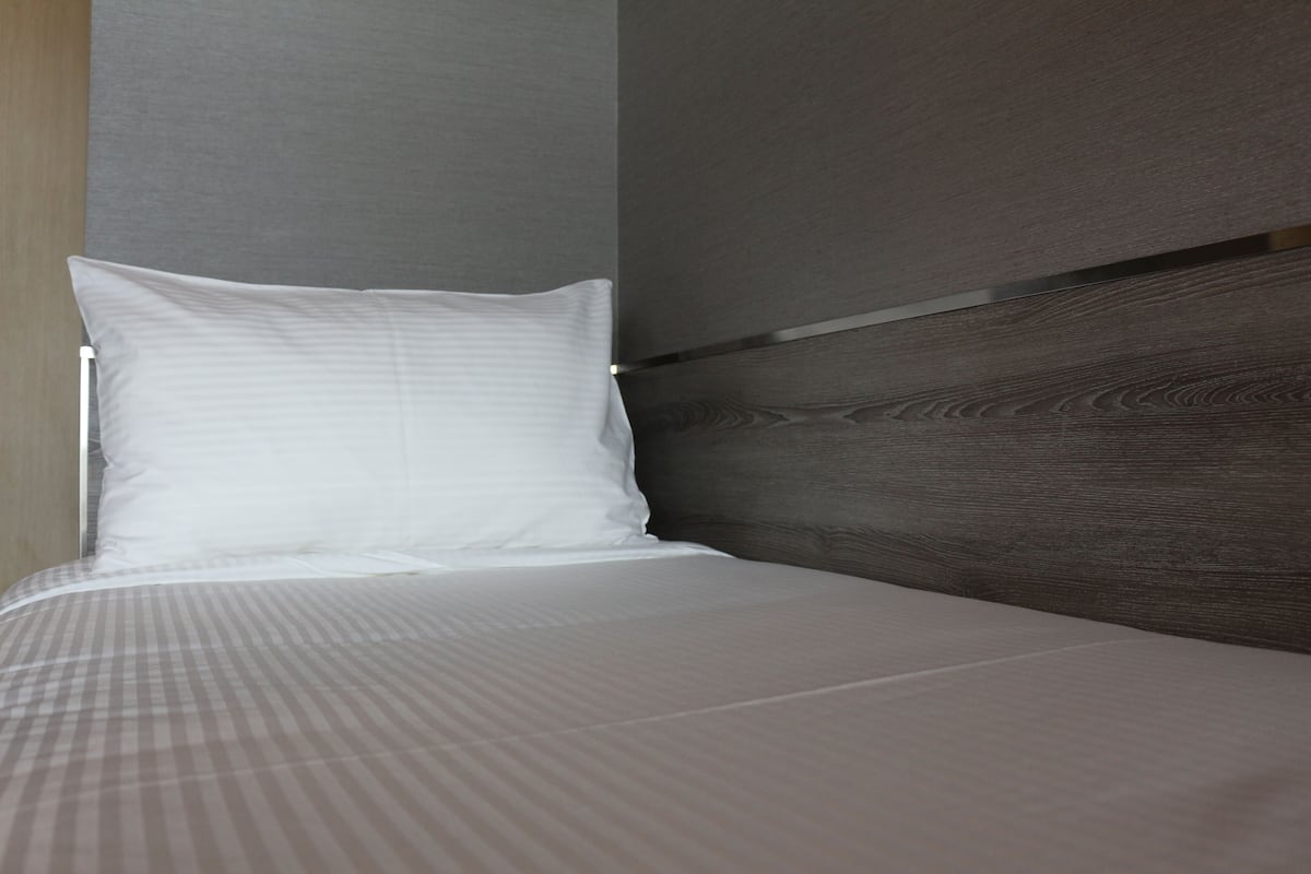 Una cama bien hecha con un almohadón blanco y una colcha a cuadros.