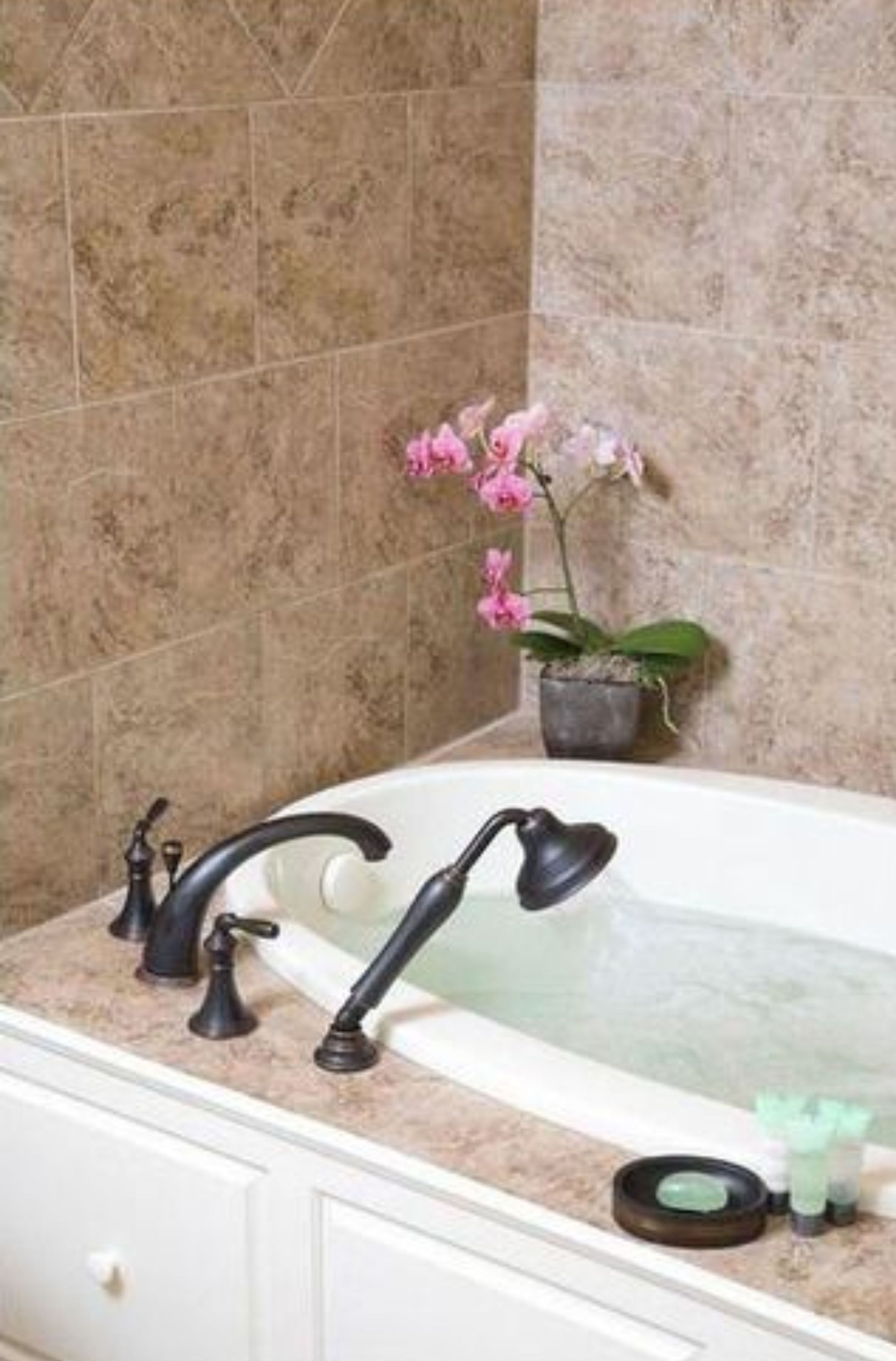 A bathroom with a bathtub, two black faucets, a potted orchid, and a small green soap dish.
