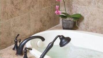 A bathroom with a bathtub, two black faucets, a potted orchid, and a small green soap dish.
