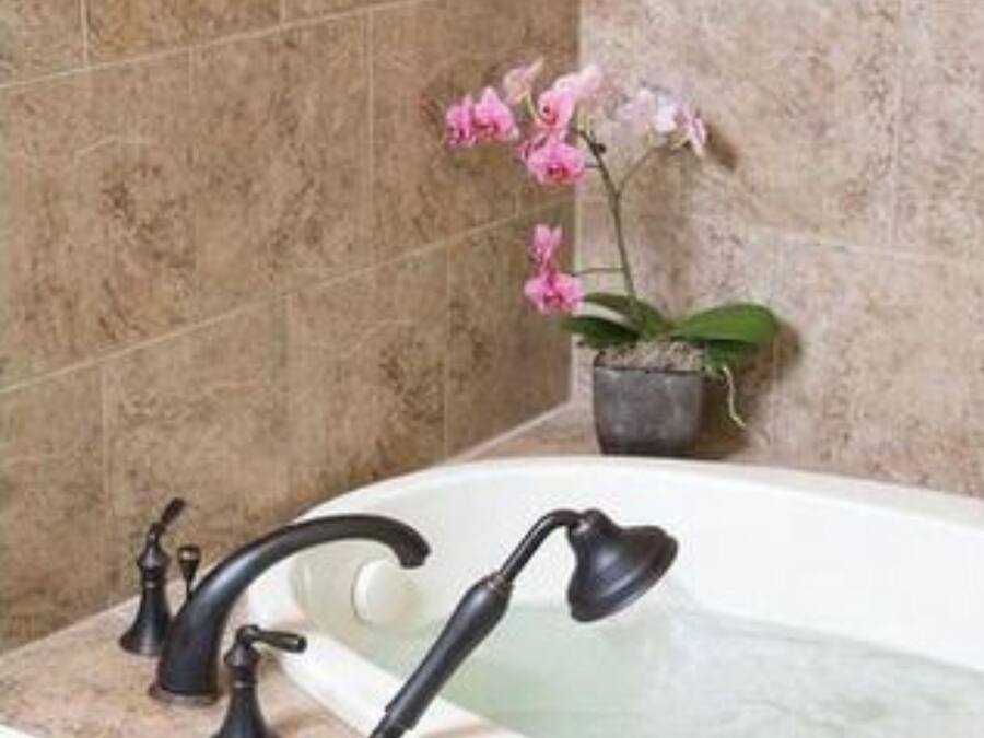 A bathroom with a bathtub, two black faucets, a potted orchid, and a small green soap dish.