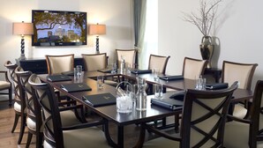 Un salón de conferencias con una gran mesa, sillas, un televisor y un florero con ramas.