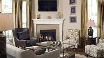 A living room with a fireplace, leather armchair, patterned armchair, and a television mounted on the wall.