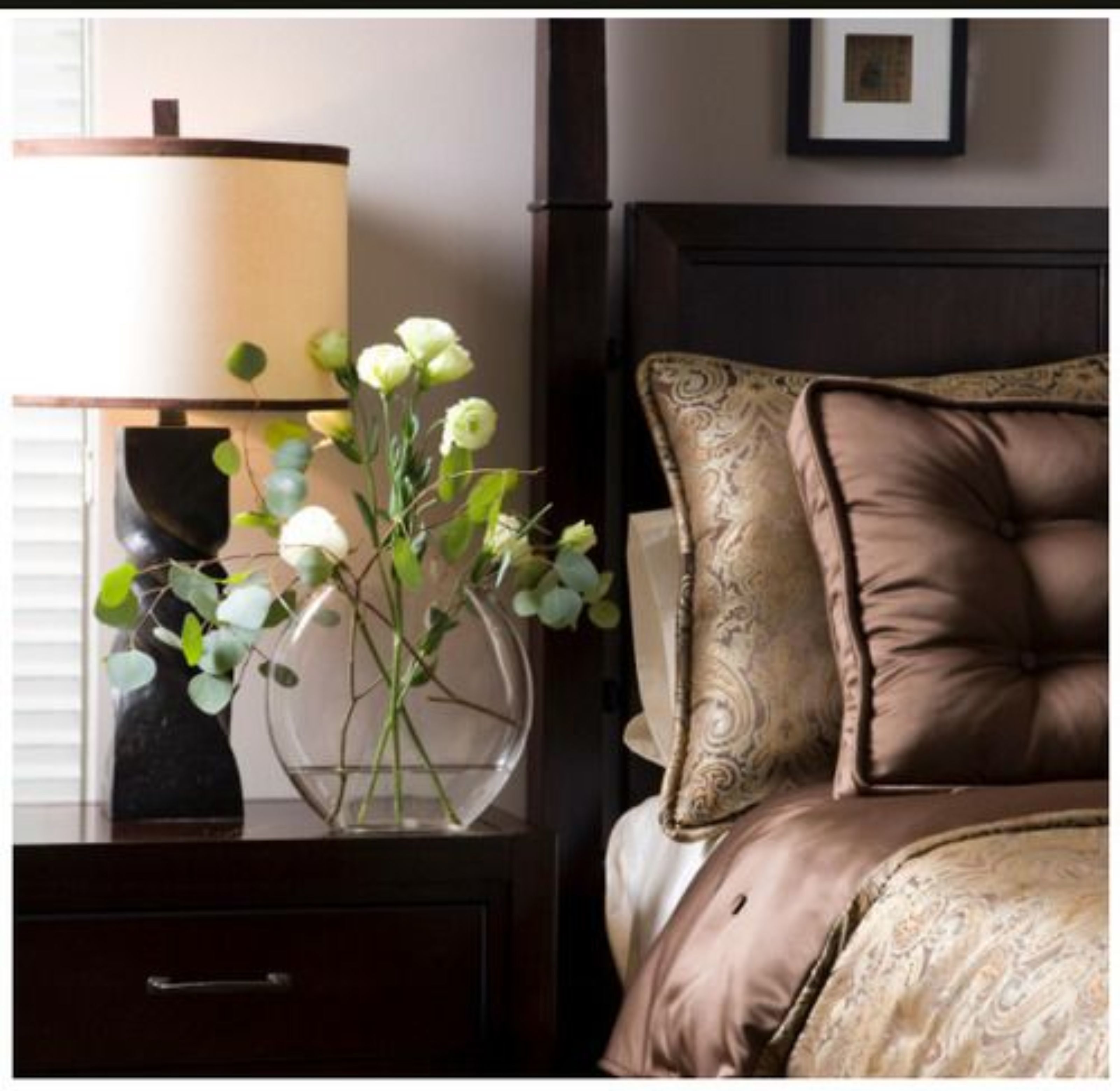 A bedroom with a bed, a nightstand, a lamp, and a vase with flowers.